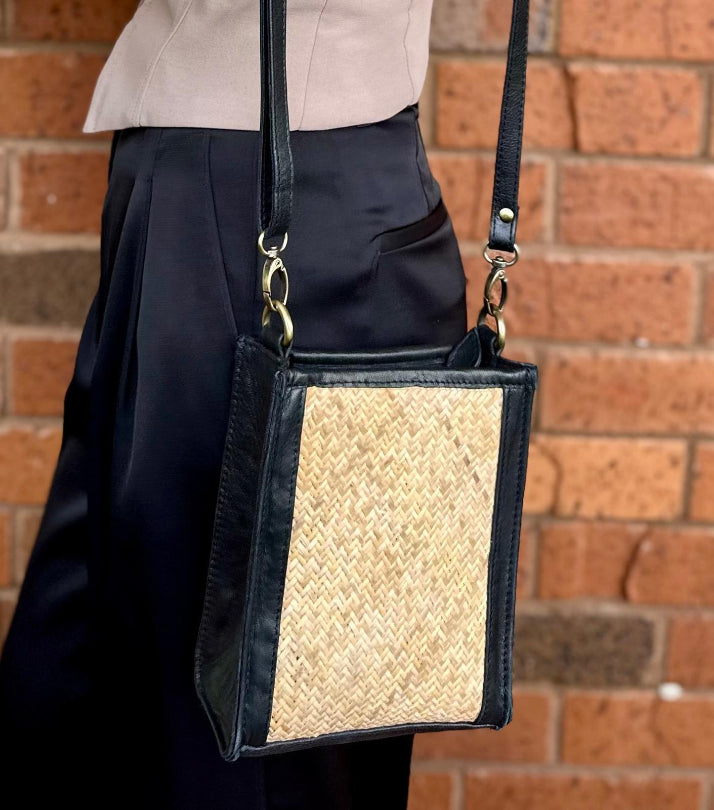 Person wearing a black handbag with a woven pattern against a brick wall.